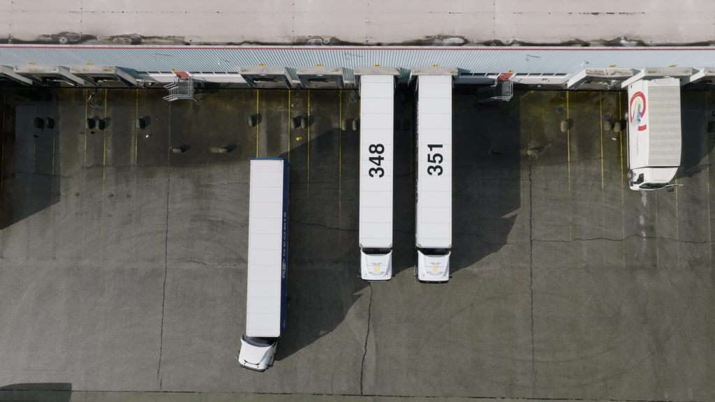 twee vrachtwagens staan bij een loading dock, eentje rijd weg